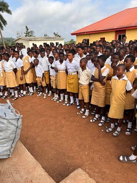 Rows of pupils lined up on a school field beside sacks of school supplies